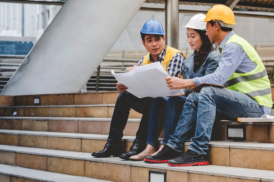 Three construction workers sitting on stairs looking at a drawing